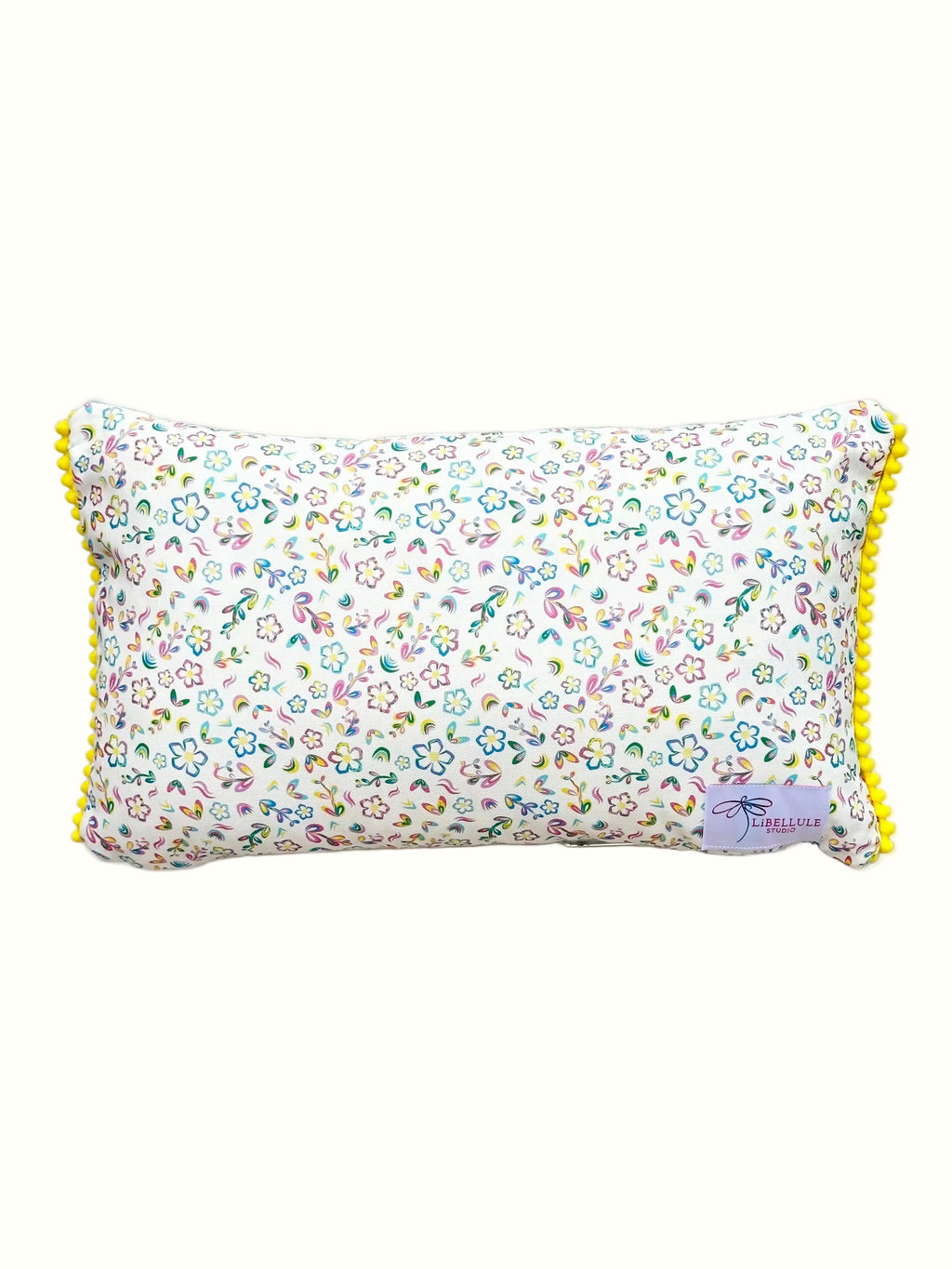 A rectangular lumbar pillow with a dense multicolor floral print on a white background, finished with bright yellow pom-pom trim along the edges.