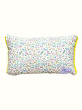 A rectangular lumbar pillow with a dense multicolor floral print on a white background, finished with bright yellow pom-pom trim along the edges.