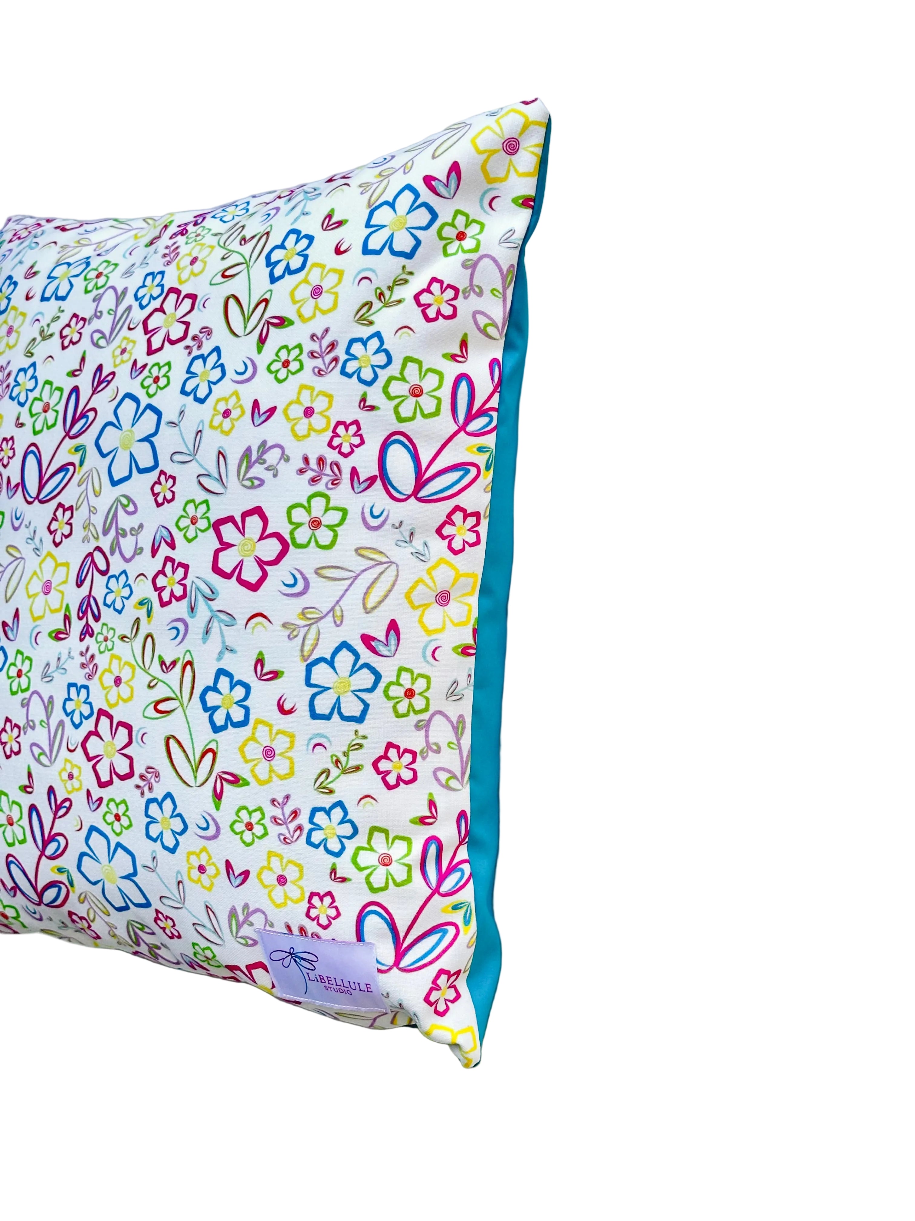 A square decorative pillow with a colorful floral and bunny pattern on a white background, featuring a solid turquoise blue fabric edge, shown against a light gray background.